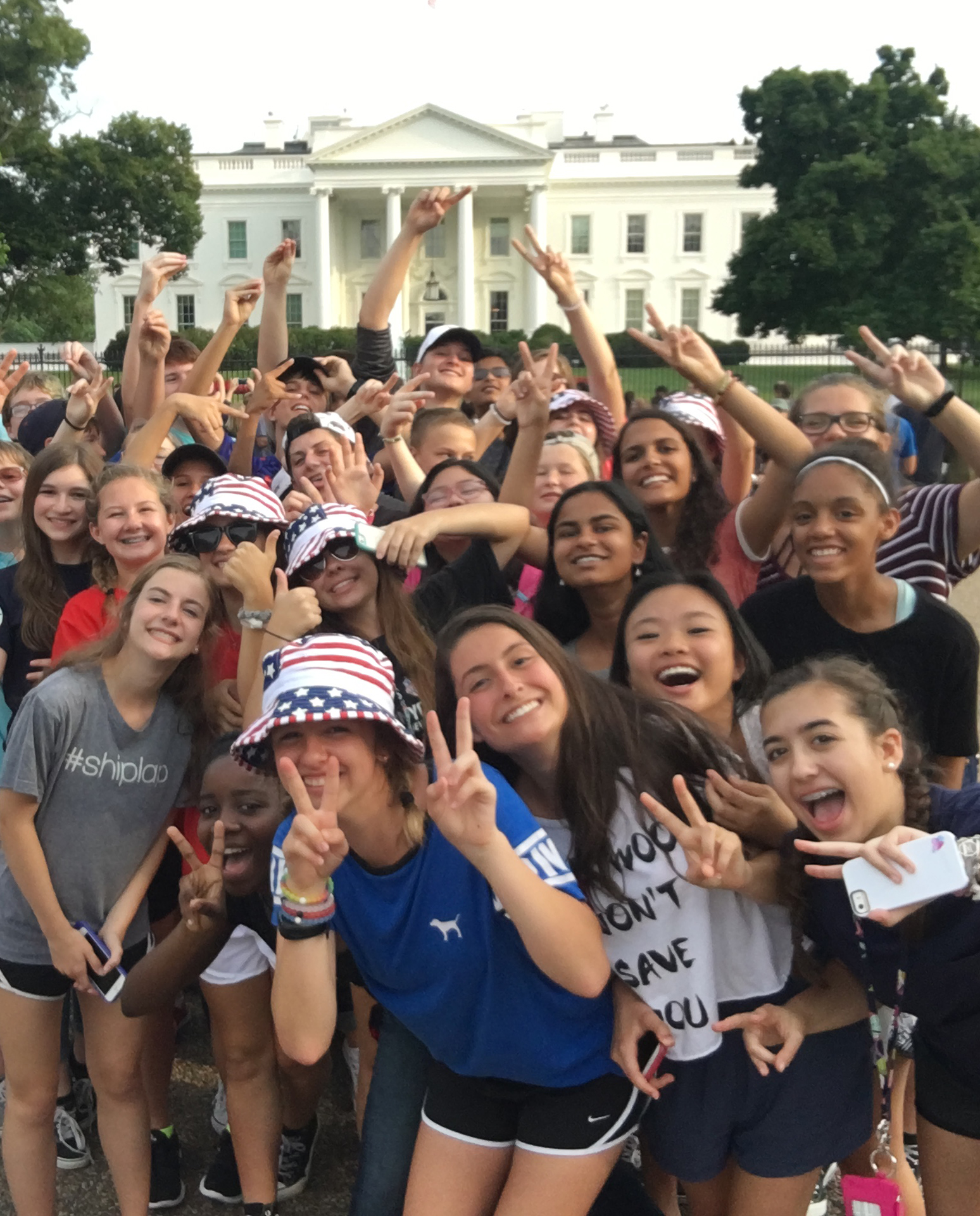 Group of middle school students holding up peace signs standing in front of the White House in Washington DC