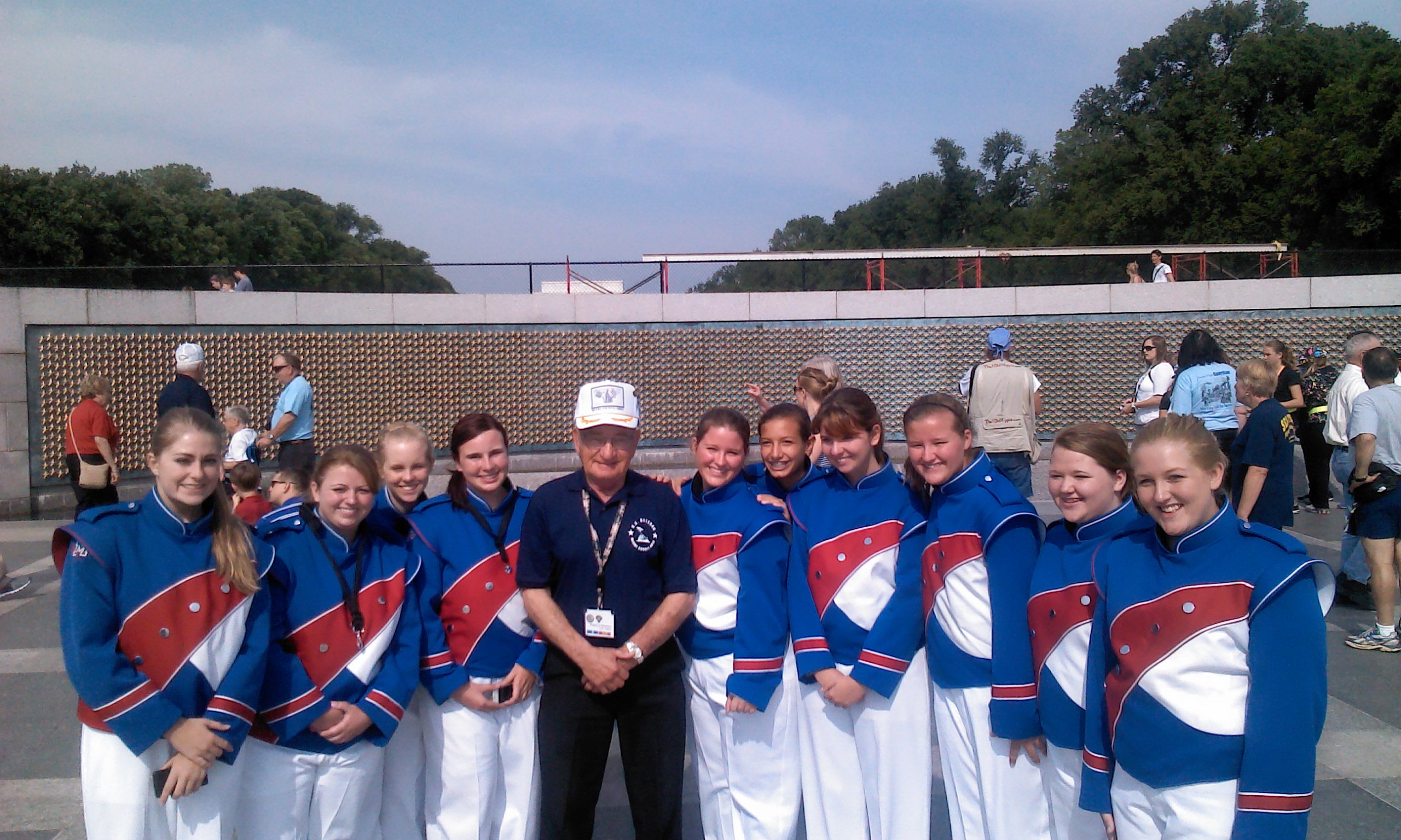 Girls in marching band uniforms posing in photo with WWII Veteran