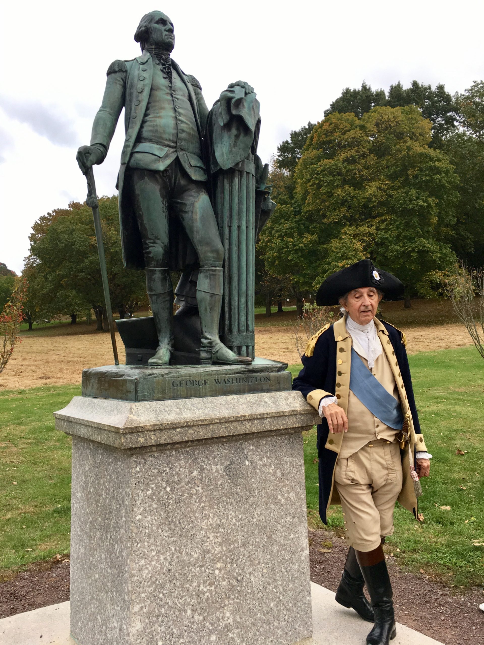 a man dressed in old colonial cloths standing next to George Washington statue