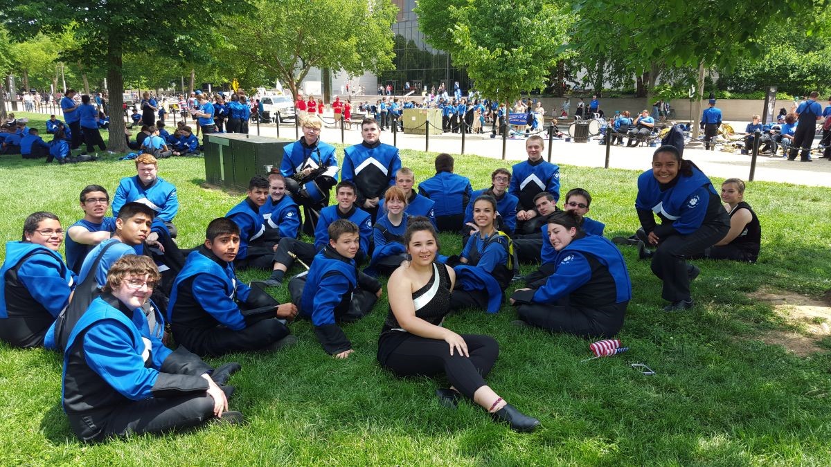 High school students in marching band uniforms sitting on grass posing for photo