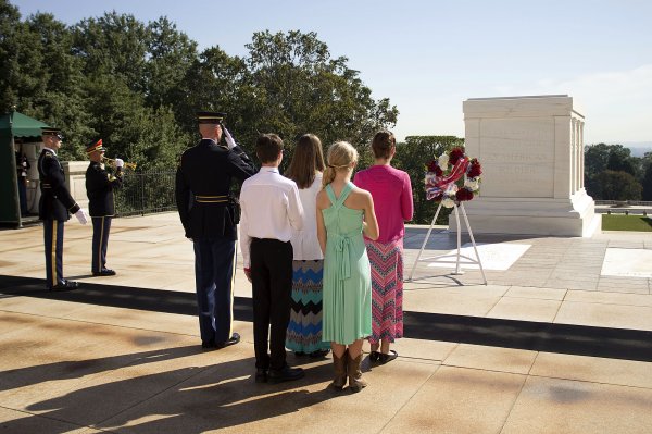 Family and soldiers standing in front of a tomb participating in memorial service
